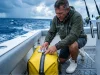 How to Waterproof Fishing Bags Before Salt Takes Them Out Angler maintaining the waterproof YKK zipper on a yellow Simms tackle bag on a wet boat deck.
