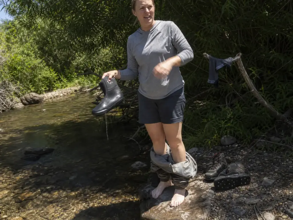 Angler holding a damp neoprene bootie, bare foot wrinkled from sweat trapped inside breathable waders