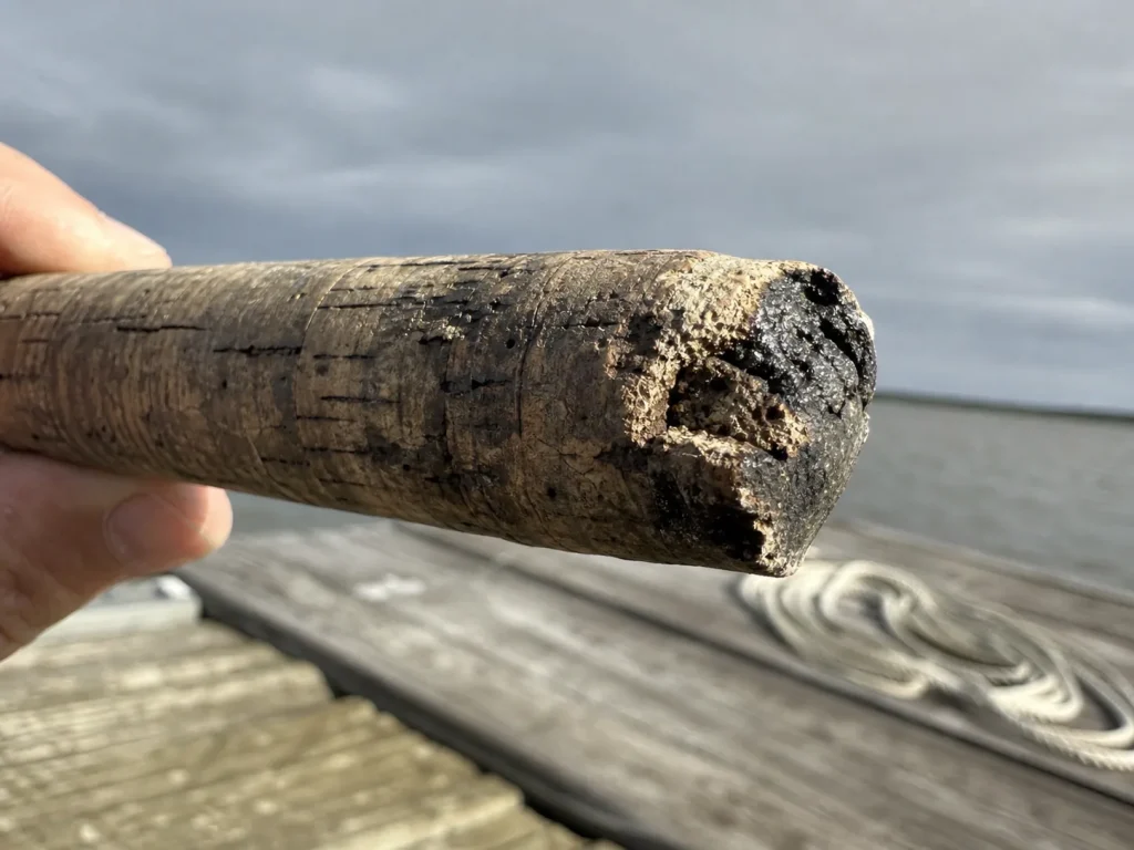 Worn pitted and stained cork rod handle showing cork rot and chipping near the reel seat
