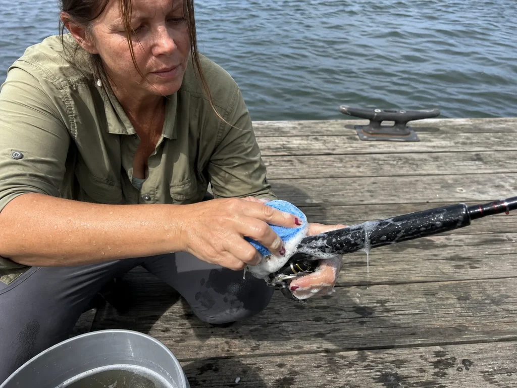 Angler scrubbing an EVA foam rod grip clean with a sponge at the dock after a fishing trip
