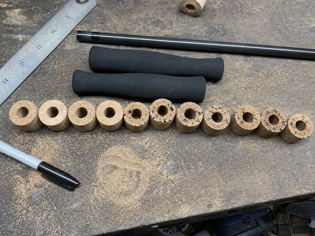 Loose cork rings and black EVA foam grips laid out on a workbench comparing rod handle material cost
