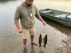 4 Fish Stringer Mistakes That Spoil Your Catch Fast Angler holding rope fish stringer with three bass in shallow lake water