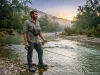 Fly Fishing or Spin Fishing for Beginners? Honest Answer Fly fishing vs spin fishing — angler choosing between two rods at a river's edge at dawn