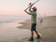 Outer Banks Surf Fishing Spots That Actually Produce Surf angler casting into the Outer Banks surf at dawn with Cape Hatteras lighthouse in background