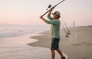 Outer Banks Surf Fishing Spots That Actually Produce Surf angler casting into the Outer Banks surf at dawn with Cape Hatteras lighthouse in background