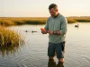 5 Popping Cork Rig Mistakes That Lose Inshore Fish Angler rigging a popping cork on a Louisiana marsh flat at dawn with redfish tailing in background