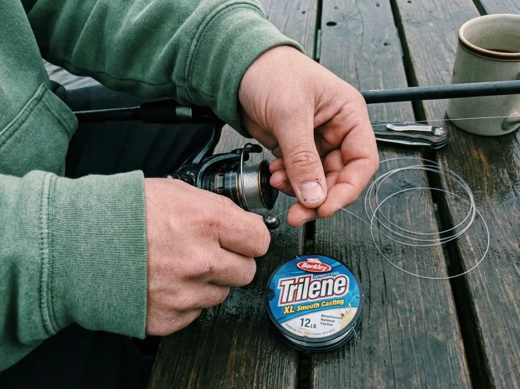Hands spooling monofilament line onto a spinning reel while setting up beginner fishing line