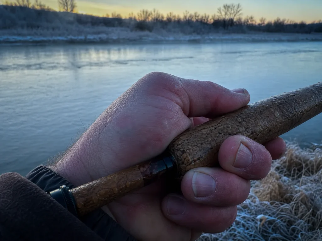Bare cold hand gripping a wet cork rod handle at frosty dawn showing cork stays warm to the touch