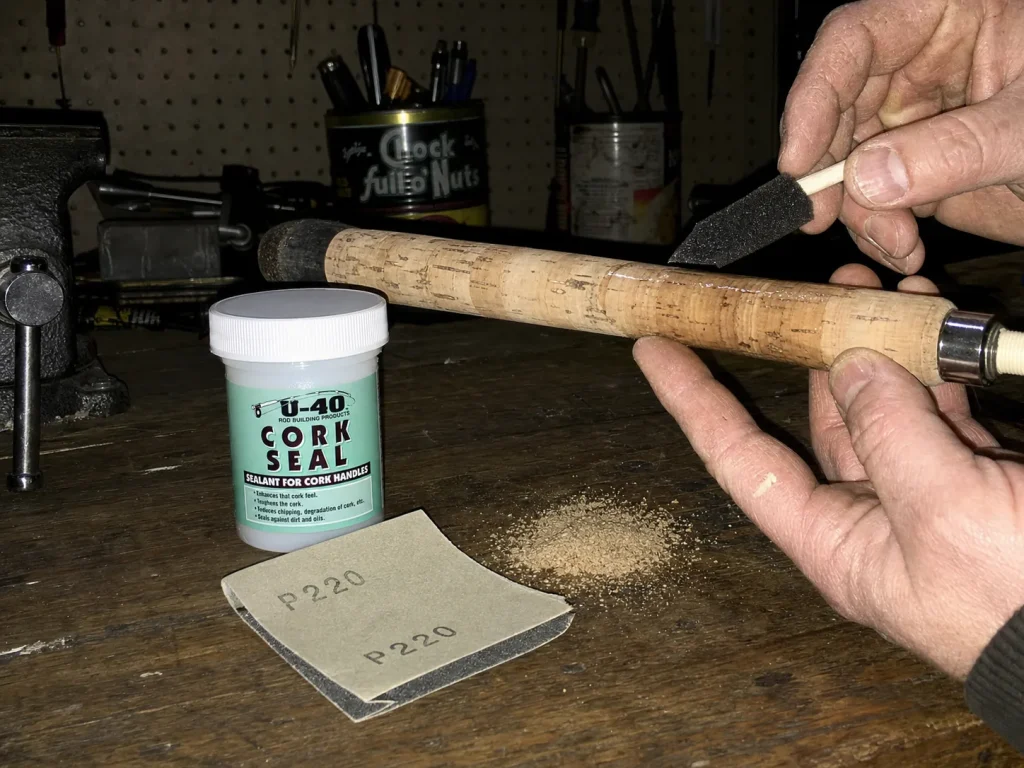 Applying U-40 cork sealant to a repaired rod handle on a workbench with sandpaper and filler
