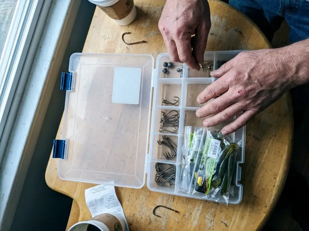 Hands organizing an open tackle box, separating soft plastics from hooks to prevent rust
