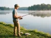 Best Beginner Fishing Setup Under $100 Ready to Fish Beginner angler holding a Shakespeare Ugly Stik GX2 spinning combo at a calm lake bank at dawn
