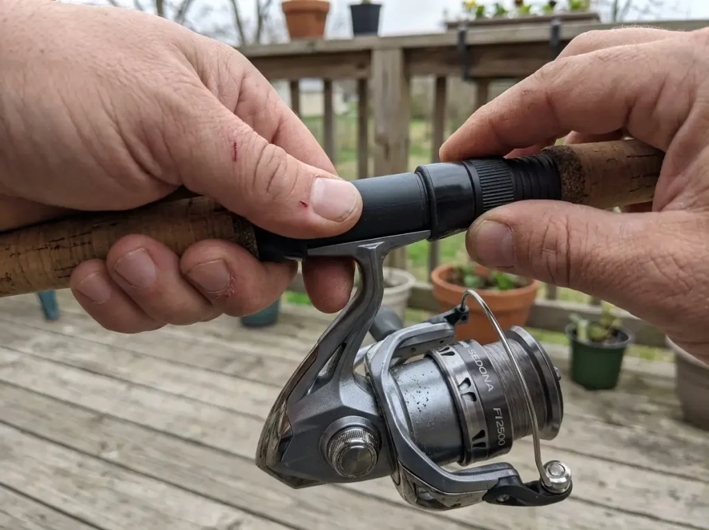 Hands seating a spinning reel into the reel seat under a fishing rod