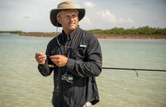 Fishing Apparel and Sun Protection Beyond the UPF Tag Angler in a long-sleeve UPF fishing shirt and wide-brim hat wading shallow water in high sun