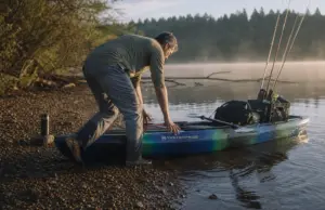 Fishing Kayak Buying Guide What Actually Matters Angler pushing a rigged fishing kayak off a gravel bank at first light