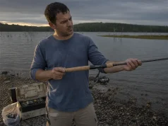 How to Choose a Fishing Rod Without Wasting Money Angler holding a spinning rod at a lake shore while deciding how to choose a fishing rod