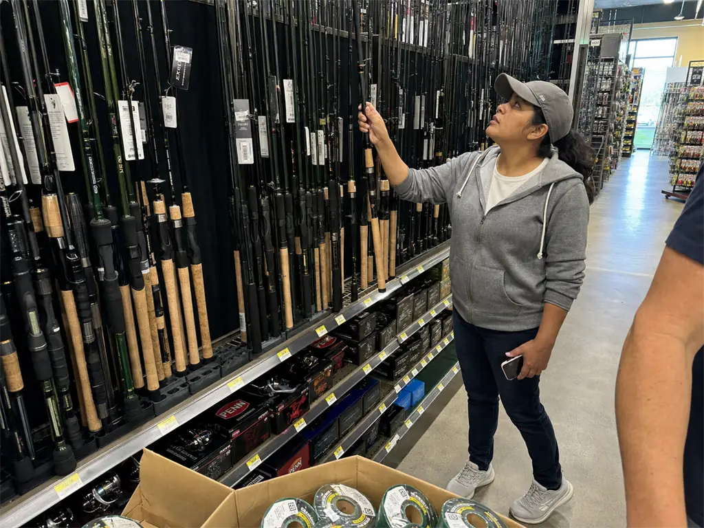 Rows of fishing rods on a tackle shop rack while a shopper decides which one to pick