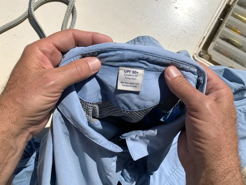 Close-up of a UPF rating tag inside a fishing shirt collar held open in bright sun