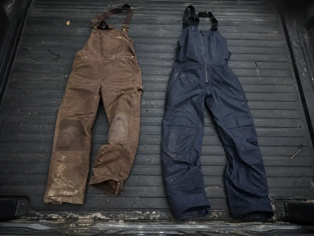 Budget insulated work bib and premium fishing bib laid side by side on a truck tailgate for comparison
