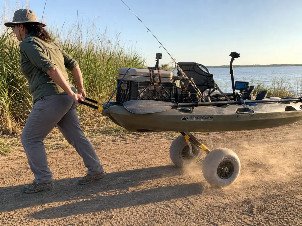 Angler wheeling a fully loaded fishing kayak to the water on a kayak cart