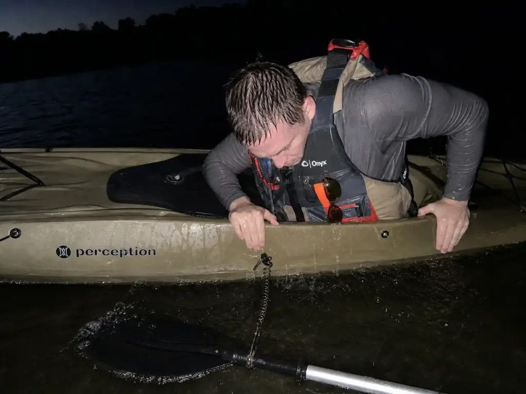 Kayak angler practicing a deep water re-entry at dusk wearing a fishing PFD