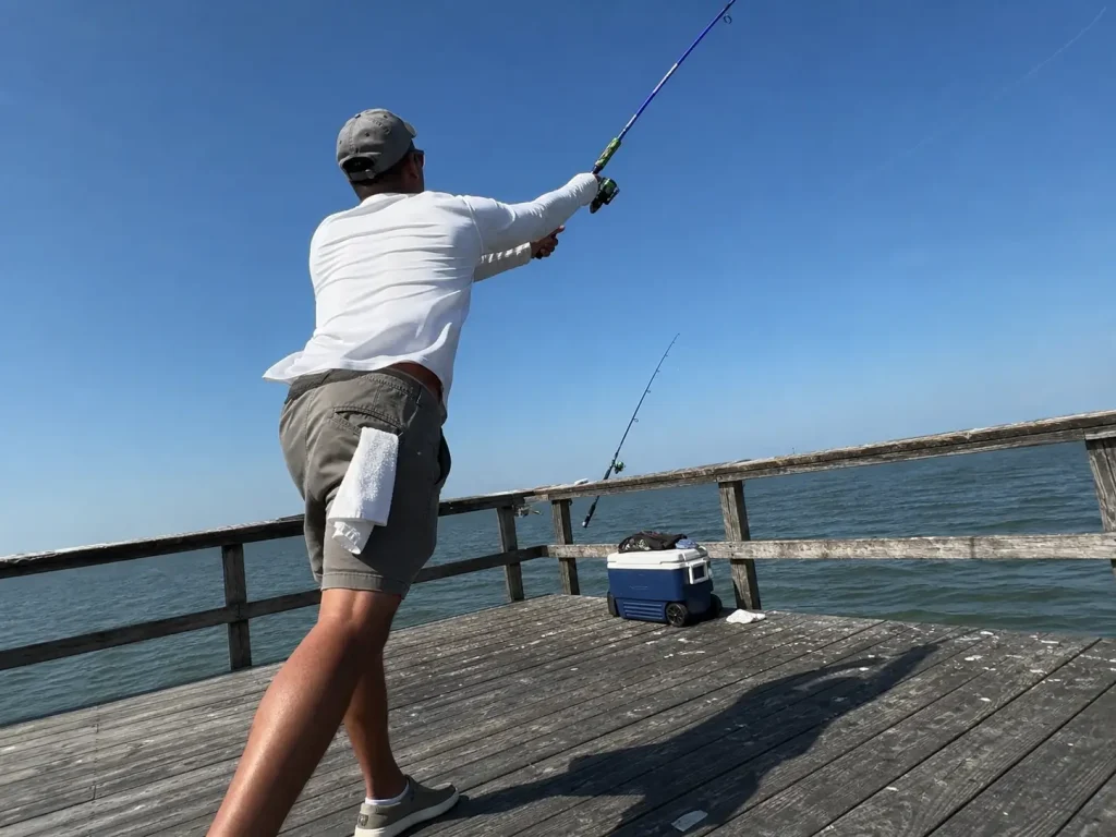 Angler casting a 7 ft medium spinning rod from an open pier in hard midday sun