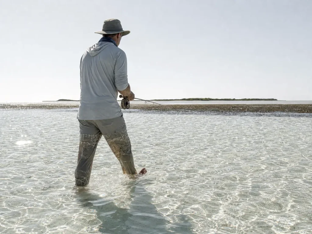Angler wading a white sand flat at midday with strong UV reflection off shallow water