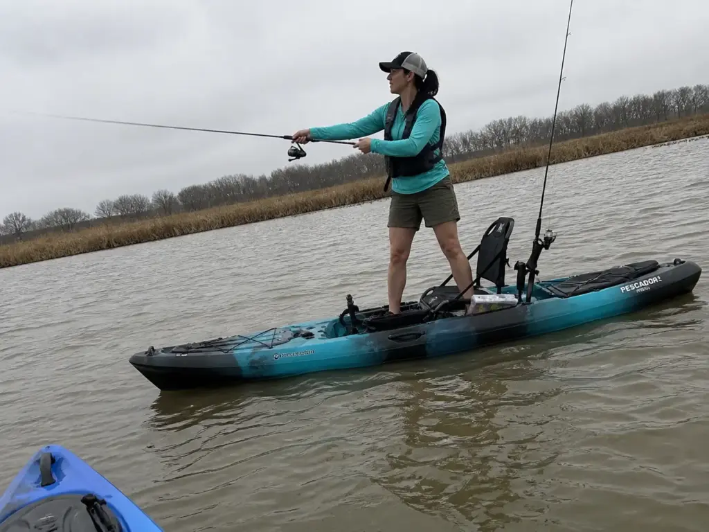 Angler standing to cast from a wide-beam fishing kayak on flat water
