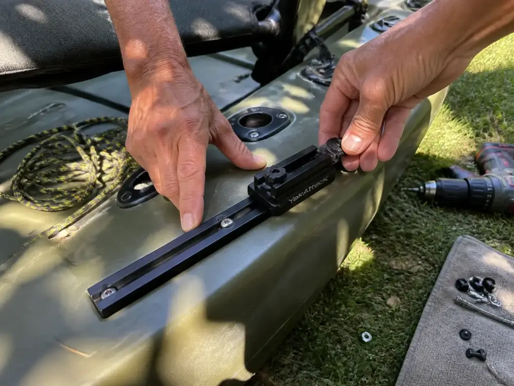 Hands sliding a rod holder mount along a kayak gear track during rigging