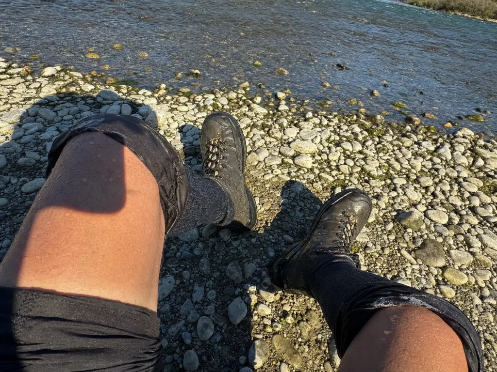 Wet wading legs in tall moisture-wicking socks and wading boots on a sunlit river gravel bar