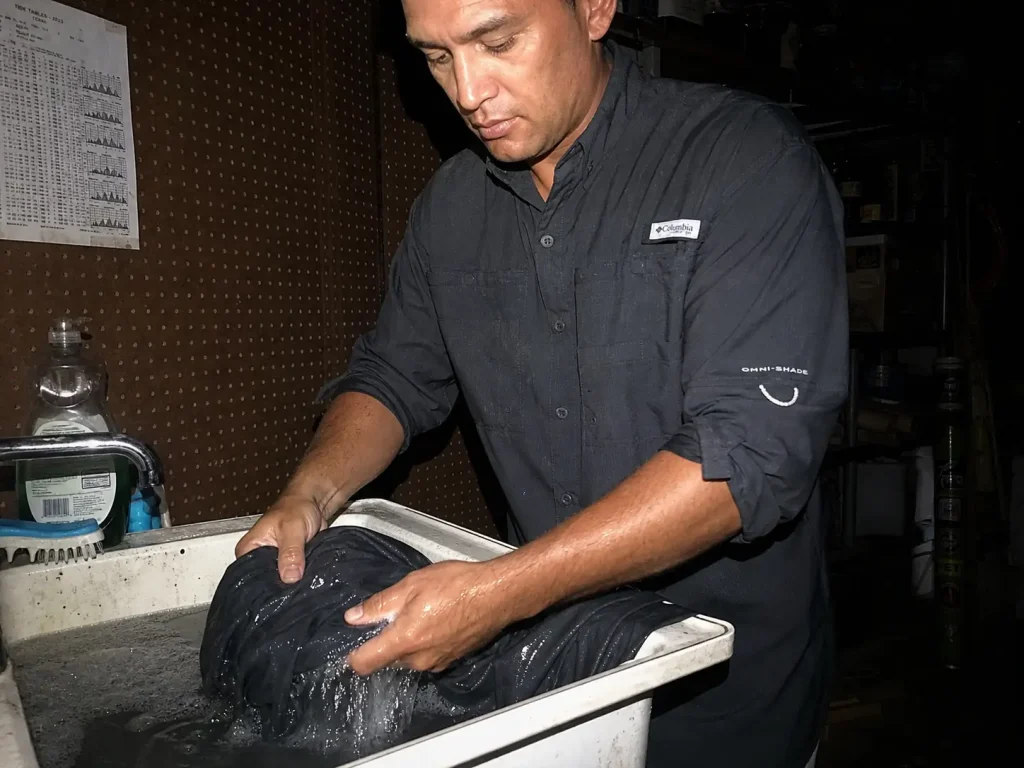 Angler rinsing a UPF fishing shirt in a utility sink at night to protect its sun protection rating