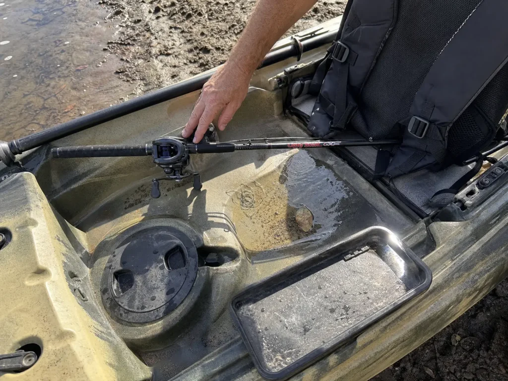 Rigged rod secured with its hook keeper across a fishing kayak deck before paddling