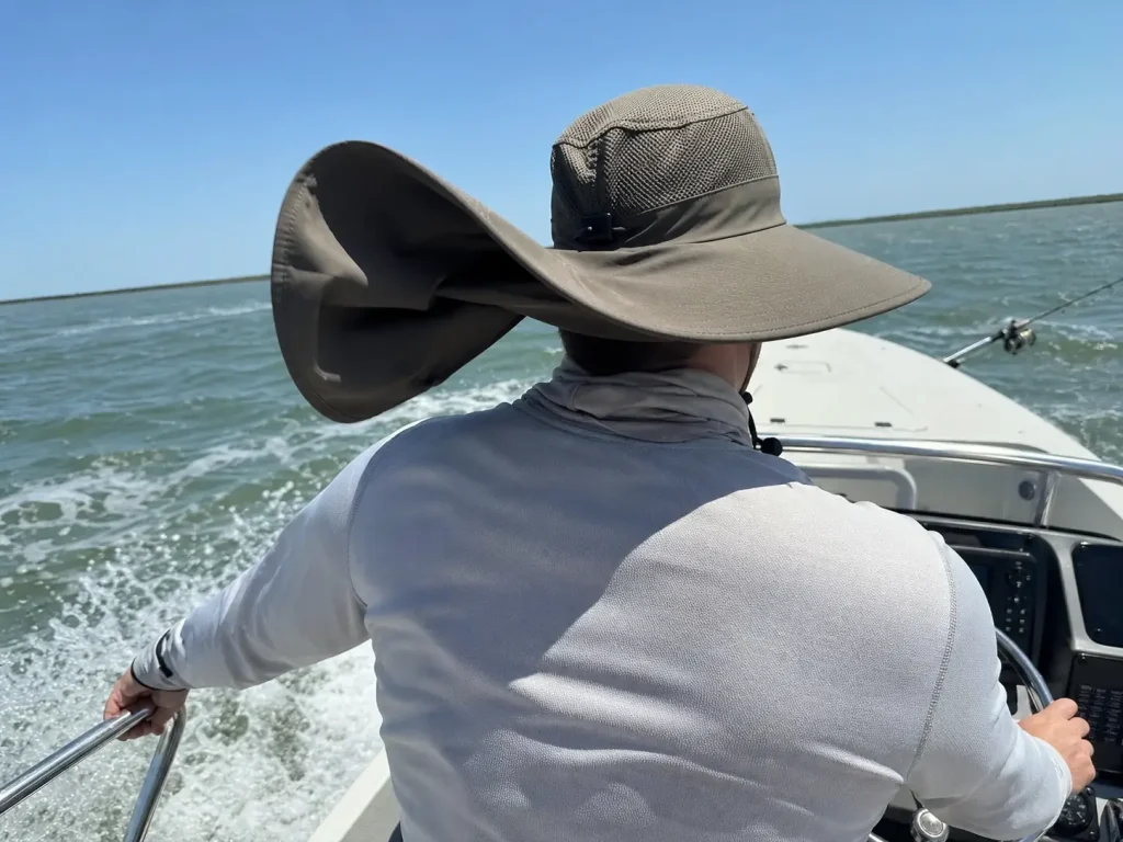 Angler in a wide-brim UPF sun hat with neck flap running a skiff across open water