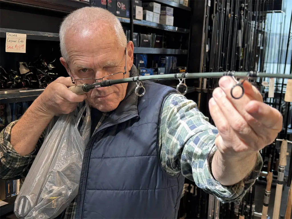 Angler sighting down the guides of a fishing rod in a shop before buying it