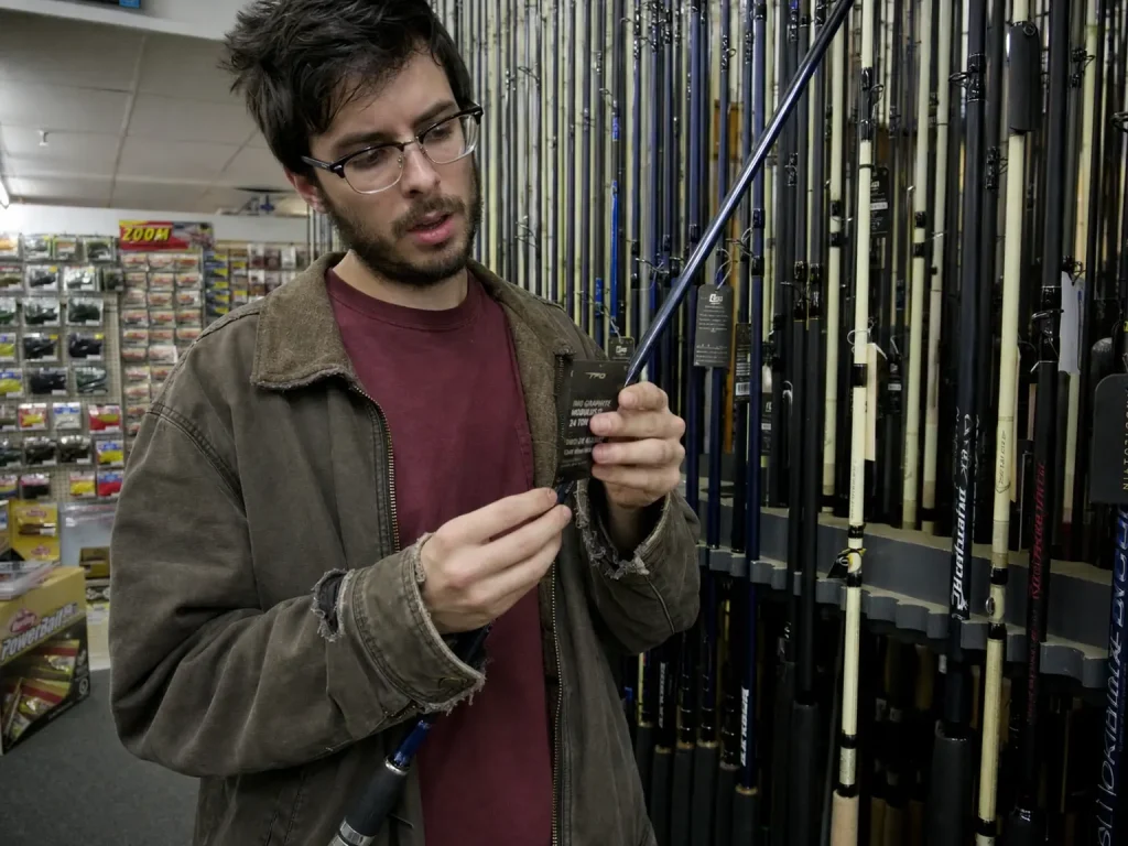 Angler reading modulus hang tags on a tackle shop rod rack while comparing blanks